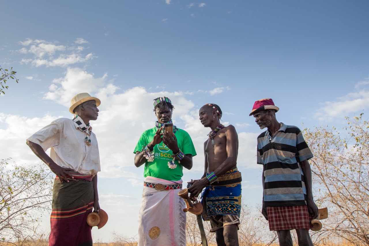 Kitabo Wele, 25, Afriscout promoter, discusses about the use of Afriscout application with a pastorialists Muda Gela, 66,  Andulsha Kefa, 45 and Kole Kilkila, 53 (right to left) in Hamer Woreda, South Omo zone, SNNPR, Ethiopia.