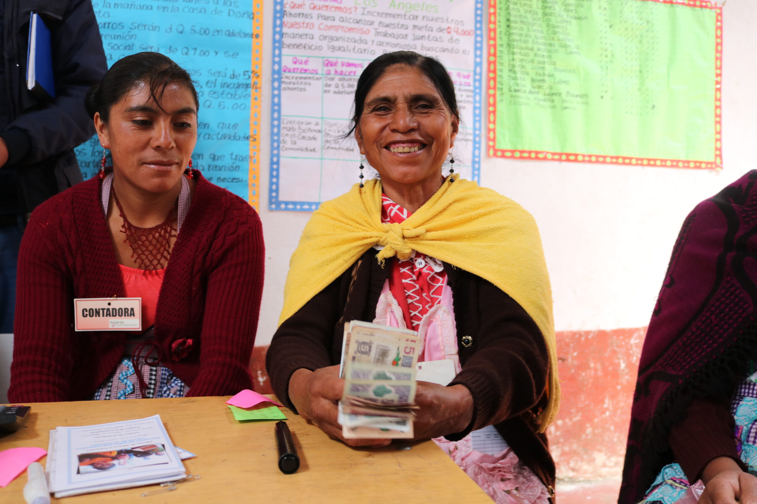 Two Guatemalan women in a savings and loans group holding money and smiling into the camera